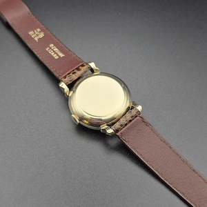 K&ouml;nnte beinhalten: Nahaufnahme einer goldfarbenen Uhr mit braunem Lederarmband. Das Zifferblatt der Uhr ist kreisf&ouml;rmig und poliert. Das Armband ist aus echtem Echsenleder und 1,6 cm breit.