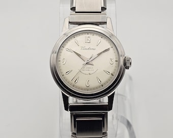 May include: A silver Vendome wristwatch with a light-coloured face. The watch has a round dial with hour markers, hands, and the brand name. The watch band is made of silver metal links. The watch has a crown on the right side.