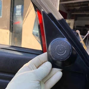 Könnte beinhalten: Nahaufnahme eines schwarzen Autotürpanels mit roter Verkleidung und einem Lautsprechergitter. Eine behandschuhte Hand hält das Panel.