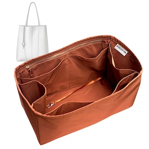 May include: A rust-colored handbag organizer with multiple compartments and a zippered top. A white tote bag is visible in the background. The organizer has a label that reads "PZEOTYN".