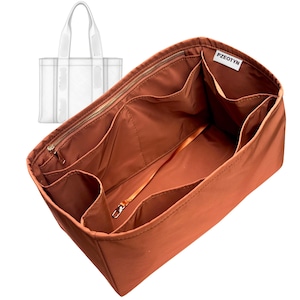 May include: A rust-colored handbag organizer with multiple compartments and a zippered top. The organizer has a light-colored strap and the brand name "PZEOTYN" is visible. A clear tote bag is in the background.