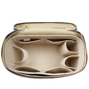 Op de afbeelding: Open, bruine cosmetische tas met een beige interieur met meerdere compartimenten en vakken. De tas heeft een ritssluiting en een goudkleurige ritstrekker. De binnenkant bevat een label met de tekst "PZEOTYN".