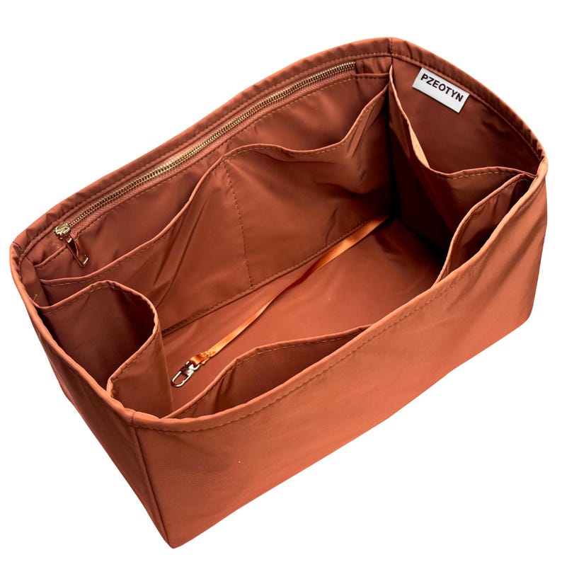 May include: A rust-colored handbag organizer with multiple compartments and a zippered top. The interior features various pockets and a strap with a metal clasp. The brand name "PZEOTYN" is visible on a small white tag.