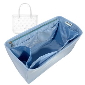 Może przedstawiać: Jasnoniebieski organizer do torebki z wieloma kieszeniami i zapięciem na zamek błyskawiczny. Organizer wykonany jest z gładkiego, satynowego materiału i posiada napis "PZEOTYN" na małej białej etykiecie. Rysunek techniczny torby typu tote znajduje się w tle.