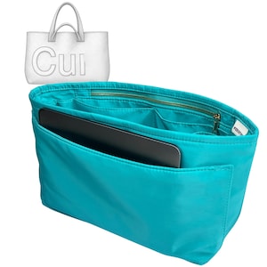 May include: A turquoise fabric handbag organiser insert featuring multiple interior compartments, a zippered pocket, and a flat black rectangular item tucked into the front sleeve. A white graphic of a tote bag with the text Cui is visible above.