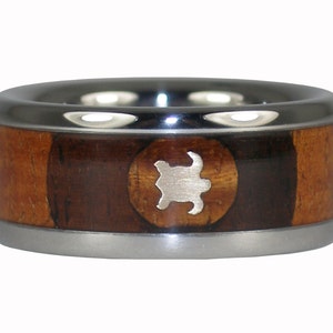 May include: A silver and wood ring featuring a silver turtle design. The ring is made from titanium and koa wood.