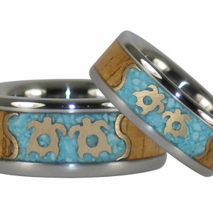 May include: Two matching titanium rings with a wood inlay and turquoise and gold accents. The rings feature a design of three sea turtles.