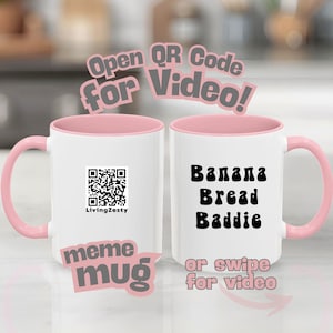 May include: Two white ceramic mugs with pink handles and interiors. One mug has a QR code and the text "LivingZesty". The other mug has the words "Banana Bread Baddie" in black. The mugs are labeled "meme mug".