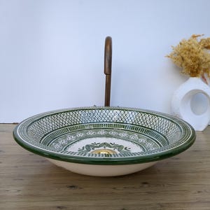 Könnte beinhalten: Ein dekoratives Keramikwaschbecken mit einem grün-weißen geometrischen Muster. Das Waschbecken hat eine breite, flache Schüssel und einen dunklen Holzarmatur. Das Waschbecken steht auf einer Holzoberfläche.