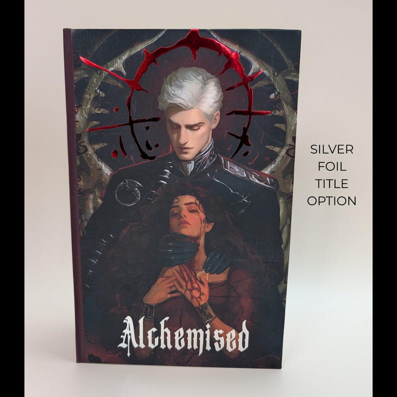 May include: A book cover with the title "Alchemised" in a gothic font. The cover art features a man with silver hair and a woman in a red dress. The text "Silver Foil Title Option" is on the right side of the cover. The background has a dark, ornate design.