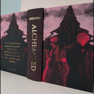Könnte beinhalten: Ein Hardcover-Buch mit dem Titel "Alchemised" von Senlinyu. Der Buchrücken ist dunkelburgunderfarben mit goldfarbenen Buchstaben. Das Cover zeigt eine dunkle, gotische Illustration mit Figuren in Rot und Schwarz und dem Text "I have warned you..."