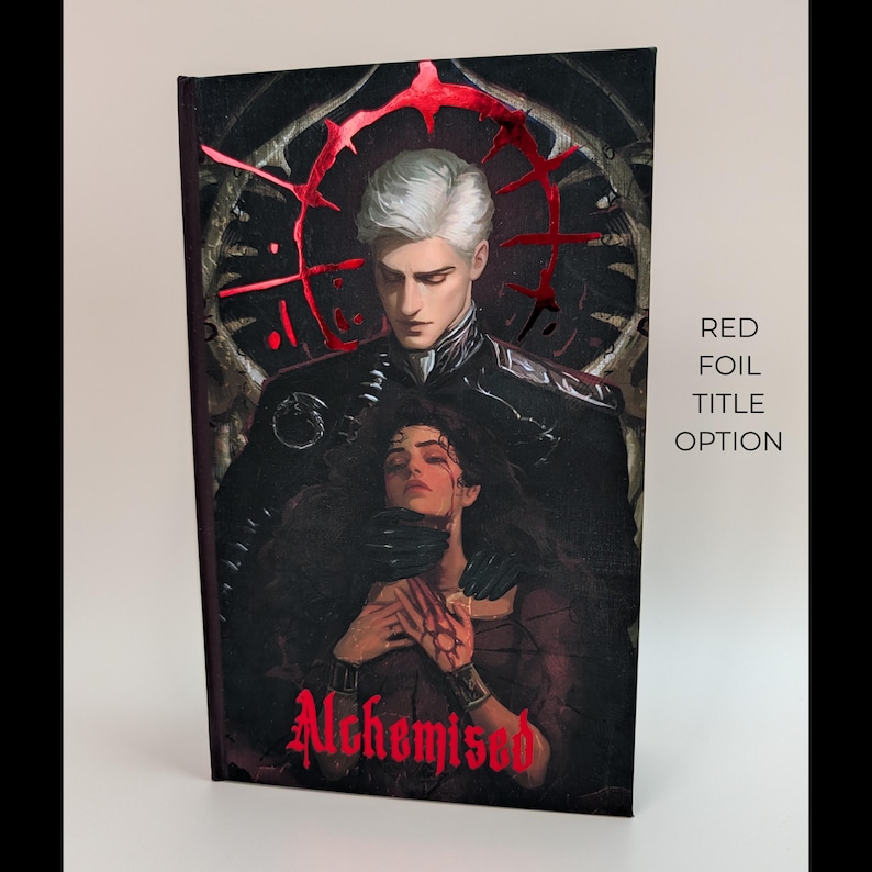 May include: A hardcover book with a dark, gothic-style cover featuring a male and female figure. The title "Alchemised" is in red foil. The text "RED FOIL TITLE OPTION" is on the right side.