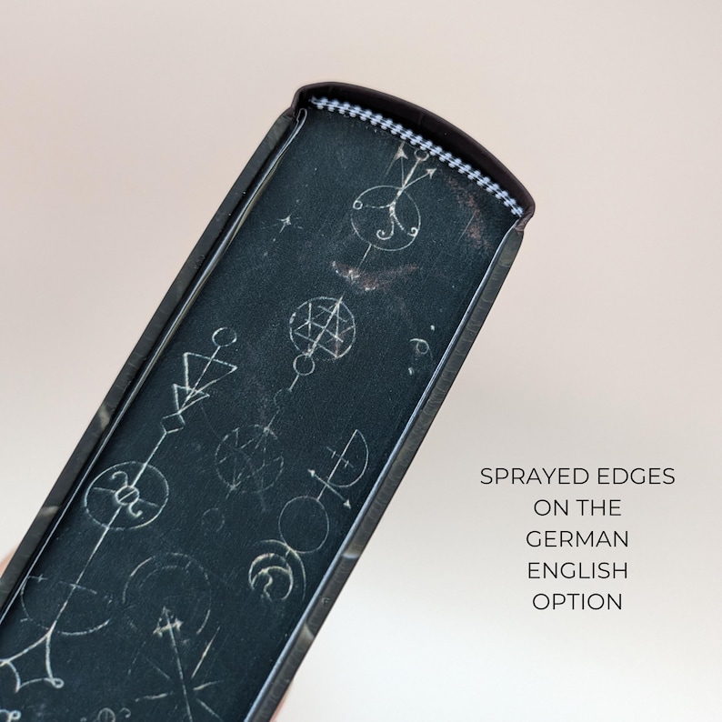May include: Close-up of a dark book spine with white geometric designs. The spine has a textured appearance and a decorative top edge. Text on the right side reads "Sprayed edges on the German English option."