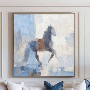 May include: Large framed abstract painting of a horse in shades of blue, grey, and brown. The artwork is displayed above a white sofa with blue velvet throw cushions. The room has a neutral colour palette with a wooden coffee table.