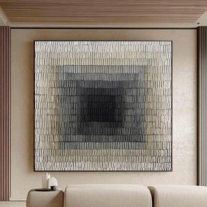 Könnte beinhalten: Große abstrakte Wandkunst mit quadratischem Design. Das Kunstwerk zeigt einen Farbverlauf, der in einem rechteckigen Muster von hellem Beige zu dunklem Grau übergeht. Das Stück ist schwarz gerahmt und hängt über einem beigen Sofa.