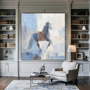 May include: Abstract painting of a horse in blue, grey, and brown tones. The artwork, with a textured finish, is displayed in a living room with bookshelves and a cream armchair. The room has a rug and a coffee table.