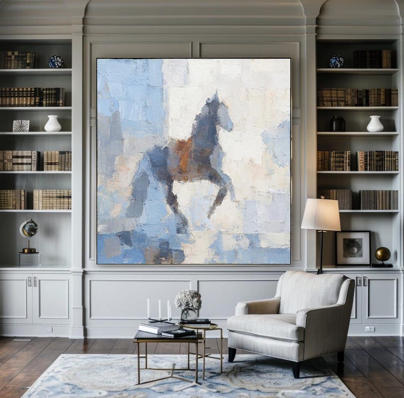 May include: Abstract painting of a horse in blue, grey, and brown tones. The artwork, with a textured finish, is displayed in a living room with bookshelves and a cream armchair. The room has a rug and a coffee table.