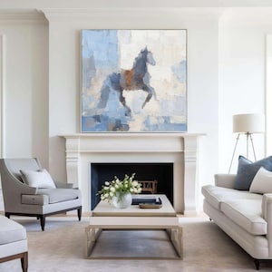 May include: Abstract painting of a horse in blue, grey, and brown tones. The artwork is displayed above a white fireplace in a living room. The framed painting adds a touch of elegance to the room. The room has a sofa and chairs.