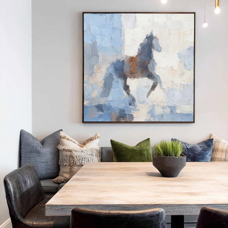May include: Large square framed abstract painting of a horse in shades of blue, grey, and brown. The artwork is displayed above a wooden dining table with decorative pillows and leather chairs.
