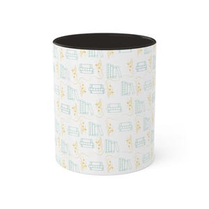 May include: White ceramic mug with a black rim and a pattern of yellow flowers and stacks of blue books.