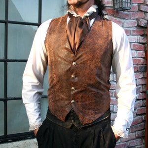 May include: A man wearing a brown leather waistcoat with a floral pattern, a white shirt with a lace trim, and black trousers. The waistcoat has a gold button closure and a brown satin cravat.