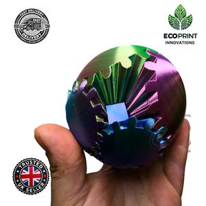 Puede incluir: Una esfera multicolor con un diseño de engranaje. La esfera está hecha de un material brillante e iridiscente y tiene una combinación de colores azul, verde y morado.