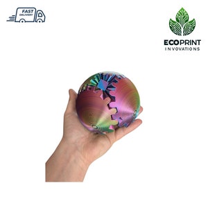 May include: A multi-coloured, iridescent sphere with a gear design. The sphere is made of plastic and is being held in a person's hand.