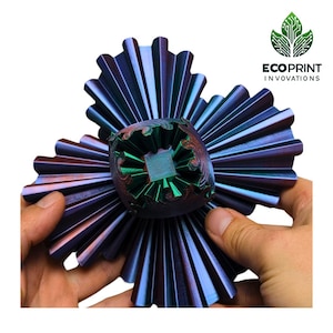 May include: A 3D printed object with a green centre and iridescent purple and blue outer layers. The object is shaped like a flower with multiple petals.
