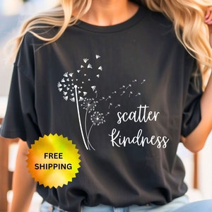 May include: Black t-shirt with a white dandelion graphic and the words "scatter kindness." The shirt is a crew neck style. A yellow and gold sticker with the words "FREE SHIPPING" is visible.