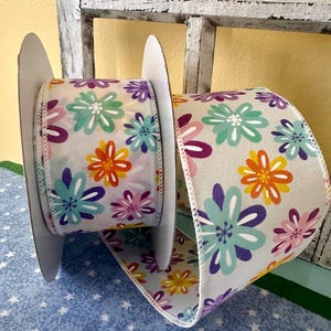 May include: Two spools of white ribbon with a colorful floral print. The ribbon features a variety of colors including purple, pink, orange, yellow, and teal.