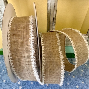 May include: A roll of brown burlap ribbon with a white frayed edge. The ribbon is on a white cardboard spool.