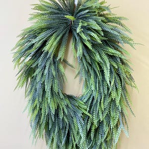 May include: An oval-shaped wreath constructed from numerous artificial fern fronds in varying shades of green. The foliage is densely packed, creating a cascading, layered appearance with a mix of light lime and deep forest green tones throughout.