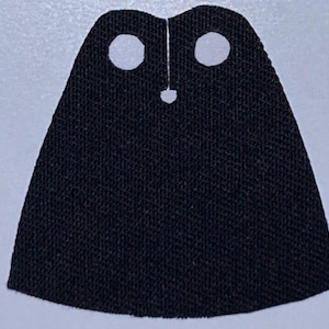 May include: Black fabric cape with two white circles and a small black button in the center.