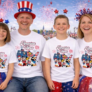 May include: A family of four wearing matching white t-shirts with the words "America Vibes" and a patriotic graphic. The background features fireworks and American flags, celebrating a festive occasion.
