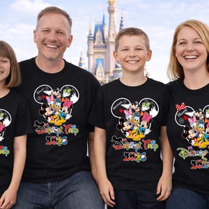 May include: Four people wearing matching black t-shirts with a colourful Disney character design and the text "Disney Trip 2023". The shirts feature Mickey Mouse ears and various Disney characters.