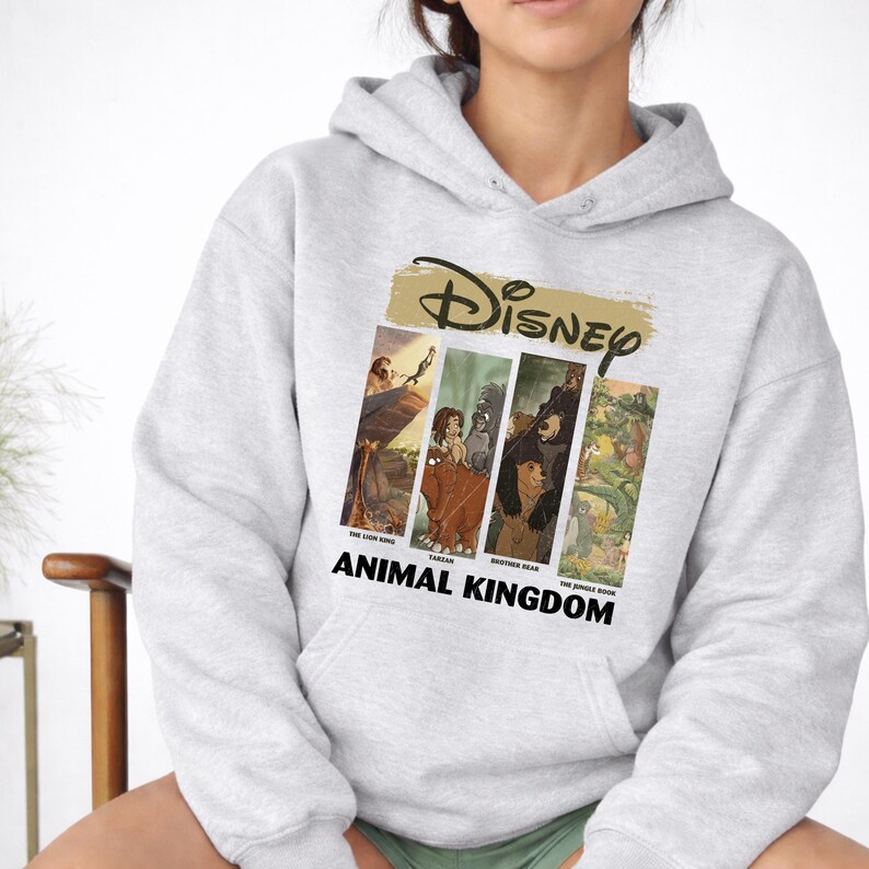 Peut inclure: Un sweat &agrave; capuche gris clair avec un motif Disney. Le motif comprend le logo Disney en or et quatre panneaux rectangulaires avec des images de "Le Roi Lion", "Tarzan", "Fr&egrave;re des ours" et "Le Livre de la Jungle". Les mots "ANIMAL KINGDOM" sont imprim&eacute;s en dessous.