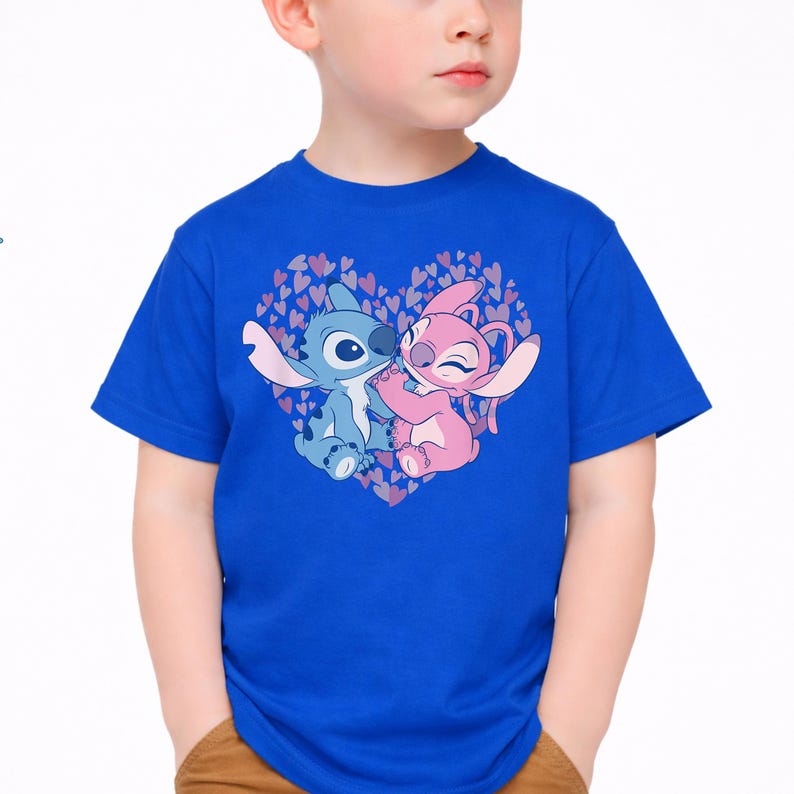 以下が含まれることがあります： ロイヤルブルーのTシャツ。リロ＆スティッチのスティッチとエンジェルのグラフィックが、小さなハートでできたハートの中に描かれています。キャラクターは青とピンクの色合いです。半袖のシャツです。