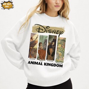 Peut inclure: Sweat-shirt blanc avec un motif Disney. Le logo "Disney" dor&eacute; est au-dessus de quatre panneaux avec des illustrations de "Le Roi Lion", "Tarzan", "Fr&egrave;re des ours" et "Le Livre de la Jungle". Les mots "Animal Kingdom" sont imprim&eacute;s en dessous.