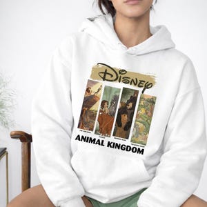 Peut inclure: Un sweat &agrave; capuche blanc avec un motif Disney. Le motif comprend le logo Disney au-dessus de quatre panneaux rectangulaires avec des images du "Roi Lion", "Tarzan", "Fr&egrave;re des ours" et "Le Livre de la Jungle". Les mots "ANIMAL KINGDOM" sont imprim&eacute;s en dessous.