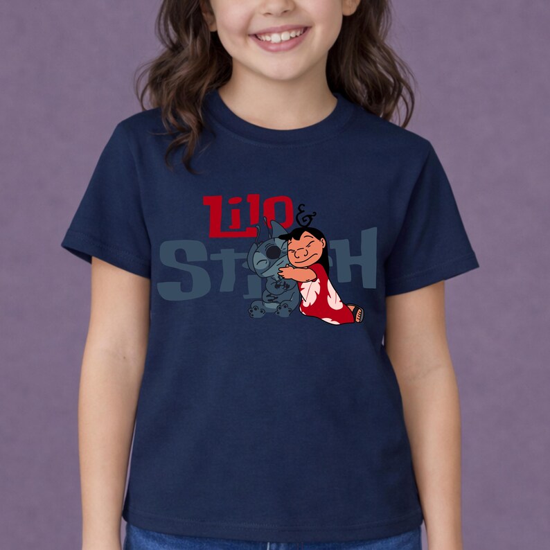 K&ouml;nnte beinhalten: Ein dunkelblaues T-Shirt mit kurzen &Auml;rmeln und einer Grafik der sich umarmenden Figuren Lilo und Stitch. Der Schriftzug Lilo & Stitch ist in roten und grauen Buchstaben &uuml;ber den Figuren aufgedruckt. Das T-Shirt hat einen Rundhalsausschnitt.