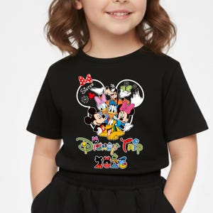 May include: Black t-shirt with a Disney Trip 2026 graphic. The design features Mickey Mouse, Minnie Mouse, Donald Duck, Daisy Duck, Goofy, and Pluto. The word "Sister" is also included in the design.