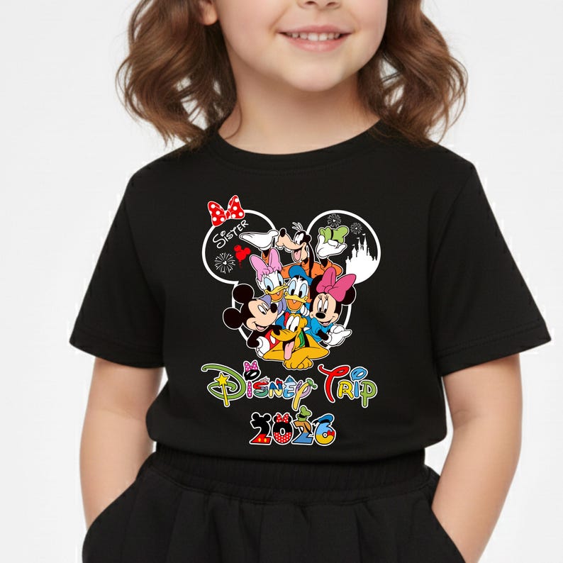 May include: Black t-shirt with a Disney Trip 2026 graphic. The design features Mickey Mouse, Minnie Mouse, Donald Duck, Daisy Duck, Goofy, and Pluto. The word "Sister" is also included in the design.