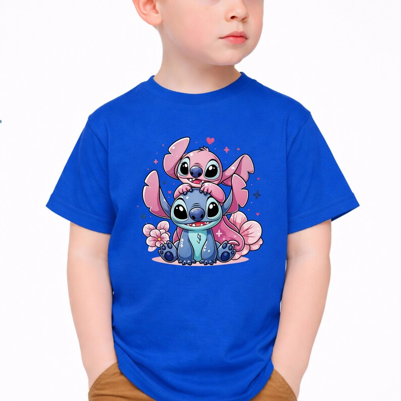 Pode incluir: Uma camiseta azul com uma ilustra&ccedil;&atilde;o de desenho animado de dois personagens, um azul e outro rosa, com olhos e orelhas grandes. Os personagens est&atilde;o empilhados um sobre o outro, rodeados por flores e cora&ccedil;&otilde;es cor-de-rosa.