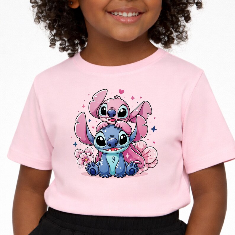 Pode incluir: Camiseta rosa claro com um desenho animado de dois personagens, um azul e outro rosa. Os personagens t&ecirc;m olhos e orelhas grandes, rodeados por flores rosas e pequenos cora&ccedil;&otilde;es. A camiseta &eacute; feita de um material macio.