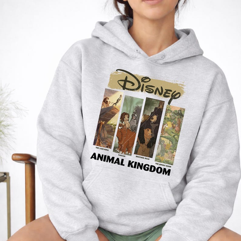 Peut inclure: Un sweat &agrave; capuche gris clair avec un motif Disney. Le motif comprend le logo Disney au-dessus de quatre panneaux verticaux avec des images de "Le Roi Lion", "Tarzan", "Fr&egrave;re des ours" et "Le Livre de la Jungle". Les mots "Animal Kingdom" sont imprim&eacute;s en dessous.
