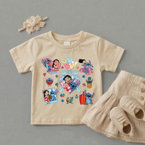 May include: A beige short-sleeved t-shirt featuring a colorful graphic print of Lilo and Stitch characters, including the text Best Friends Forever, accompanied by a matching beige hair bow, a beige tiered skirt, and beige sneakers.
