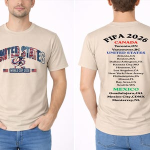 Peut inclure: T-shirt beige avec "UNITED STATES" dans un design patriotique et le texte "WORLD CUP 2026". Le dos du t-shirt liste les villes h&ocirc;tes de la FIFA 2026 au Canada, aux &Eacute;tats-Unis et au Mexique.