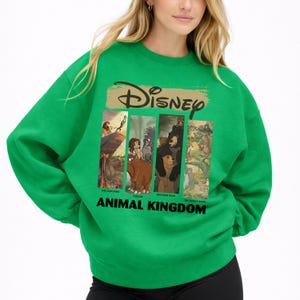 Peut inclure: Un sweat-shirt vert avec le mot "Disney" en or au-dessus de quatre images rectangulaires de personnages anim&eacute;s. Le texte "ANIMAL KINGDOM" est imprim&eacute; en noir en dessous.