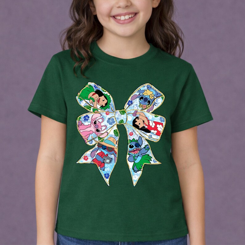 May include: A green t-shirt with a large bow design featuring cartoon characters. The bow has a blue floral pattern and gold trim, with images of Stitch, Lilo, and other characters. The shirt is worn by a child.