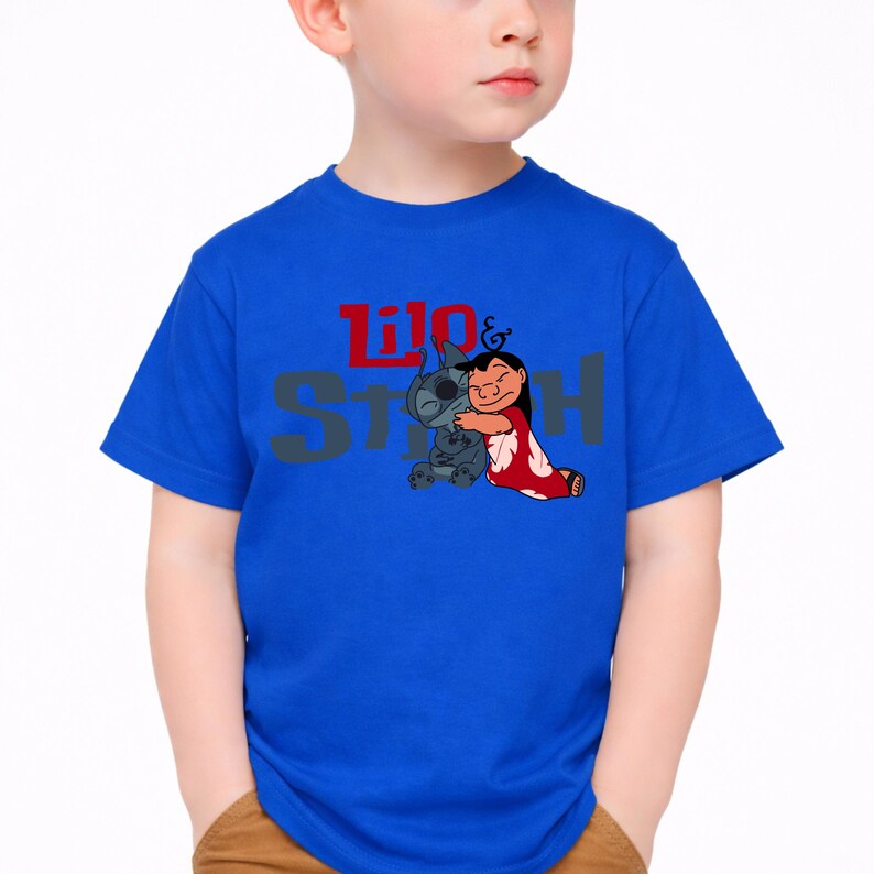 K&ouml;nnte beinhalten: Ein leuchtend blaues T-Shirt mit kurzen &Auml;rmeln und einem Grafikdruck der sich umarmenden Figuren Lilo und Stitch. Der Schriftzug Lilo & Stitch ist in Rot und Grau auf der Brust, mittig &uuml;ber der Charakterillustration aufgedruckt.